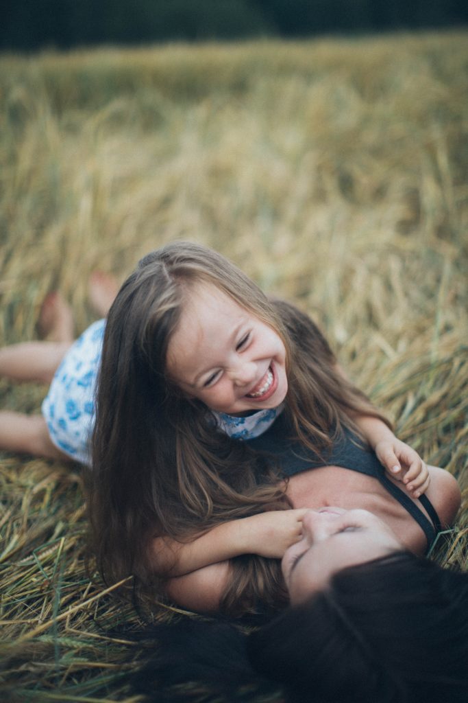 Daughter lies atop mother in the tall grass, both laughing